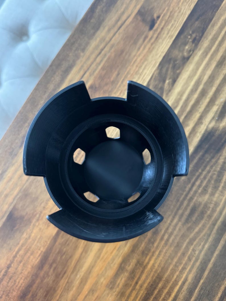 May include: Black plastic cup with six holes around the rim. The cup is designed to hold multiple items, such as pens or pencils.