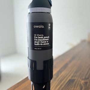 May include: A gray insulated water bottle with a black lid and a built-in straw. The bottle has the text "owala" and "Hi there. I'm leak proof. I'm insulated. And I have a built-in straw. 40 oz. (1183 mL)" printed on the side.
