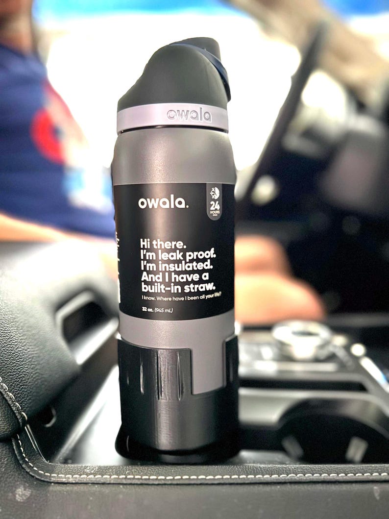 May include: A gray insulated water bottle with a built-in straw. The bottle has a black label with the text "owala." and "Hi there. I'm leak proof. I'm insulated. And I have a built-in straw. 24 hours cold. 12 oz. (345 mL)"
