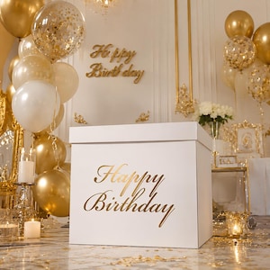 Può includere: Una grande scatola regalo quadrata bianca con il testo Happy Birthday in caratteri dorati. La scatola è circondata da palloncini dorati e bianchi, alcuni riempiti con coriandoli dorati, e una scritta da parete Happy Birthday dorata.