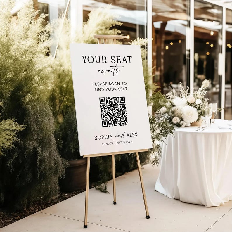 May include: A white sign on a gold easel with the text "YOUR SEAT awaits" and "PLEASE SCAN TO FIND YOUR SEAT". Below is a QR code and the names "SOPHIA and ALEX" with the date "LONDON - JULY 18, 2026".