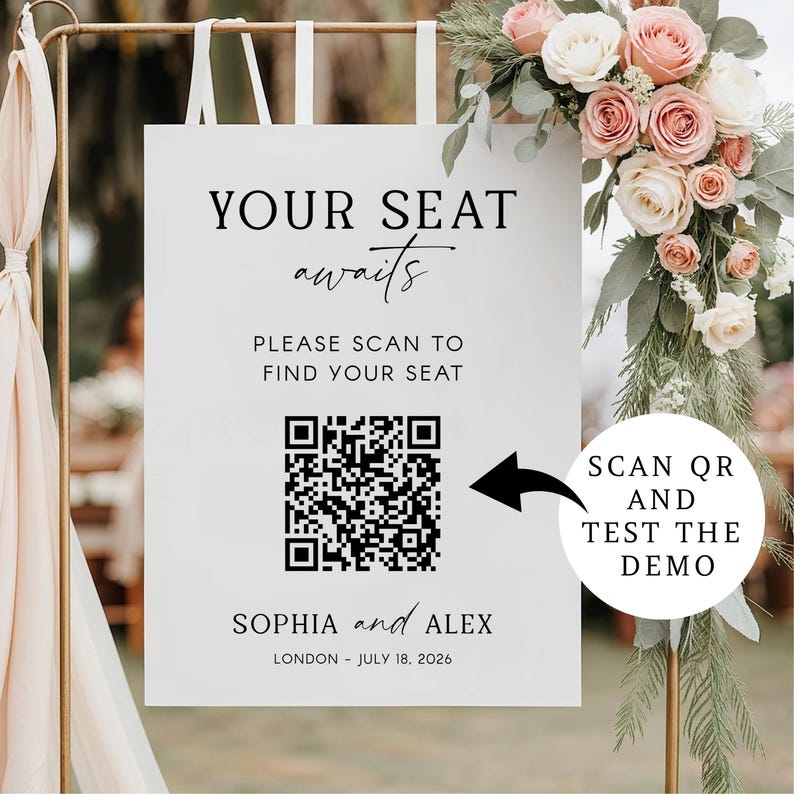 May include: A white wedding sign with black text that reads "YOUR SEAT awaits". It includes a QR code and the names "SOPHIA and ALEX" with the date "JULY 18, 2026". A floral arrangement of pink and white roses adorns the top.
