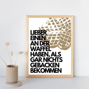 May include: A framed print with a white background and black text that reads "Lieber einen an der Waffel haben, als gar nichts gebacken bekommen."  The text is overlaid with a graphic of two golden brown waffles.