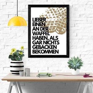 May include: A black framed print with a white background and a gold waffle graphic. The text on the print reads "Lieber einen an der Waffel haben, als gar nichts gebacken bekommen."