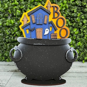 May include: A black cauldron with a blue and white haunted house and the word "BOO" in orange letters on top. The cauldron is on a wooden stand.