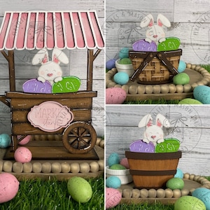 May include: A wooden Easter bunny market stall with a pink striped awning. The stall has a sign that says "Market Stand". There is a white bunny with pink ears holding purple and green eggs. The stall is on a wooden tray with green grass and speckled eggs.