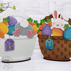 May include: Two wooden Easter baskets decorated with colorful eggs, carrots, and bunny tails. One basket is white with a purple tag that says "Easter Egg Hunt". The other basket is brown with a blue tag that says "Hoppy Easter".