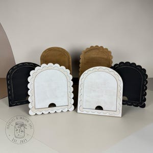May include: Wooden bookends in black, white, and tan. The bookends have a scalloped edge and a curved top. The logo "Fireflies & Mason Jars Est. 2023" is visible in the lower left corner.