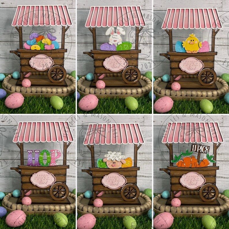 May include: Six wooden market stalls decorated for Easter. Each stall has a pink and white striped awning and a sign that says "Market Stand". The stalls are decorated with different Easter themes, including jelly beans, a bunny, a chick, the word "HOP", a sheep, and carrots.