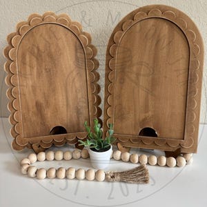 May include: A handmade wooden sign with the text "Welcome" in a playful font. The sign is painted white with a distressed finish, and features a decorative floral design in shades of pink and green. It measures approximately 12 inches wide.