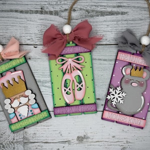 May include: Three wooden Christmas ornaments with a Nutcracker, Sugar Plum Fairies, and Mouse King theme. Each ornament has a pink, green, or purple background with white polka dots. The ornaments are decorated with glitter, paint, and fabric bows.