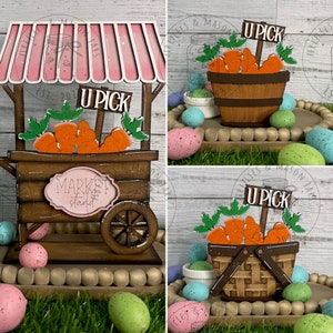 May include: A wooden market stand with a pink awning, a sign that says "U Pick", and a basket of carrots. The stand is decorated with brown and white paint and has a sign that says "Market Stand". The stand is surrounded by Easter eggs.