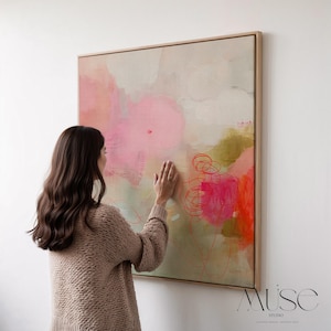 Op de afbeelding: Abstracte kunstschilderij met een houten frame. Het kunstwerk toont een mix van roze, groene en witte tinten met rode lijnaccenten. Het schilderij wordt op een witte muur getoond.