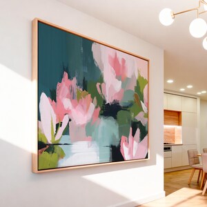 Magnolia Reverie No. 1037 by Muse Studio & Co. blush pink magnolia floral wall art with sage green and deep teal botanical brushwork printed with museum-grade giclée inks on premium gallery-wrapped cotton canvas and custom framed in natural wood with optional white, black, antique gold, or antique silver float frames to complement any decor style, styled in a coastal tropical beach home living room with airy interiors and light wood floors.