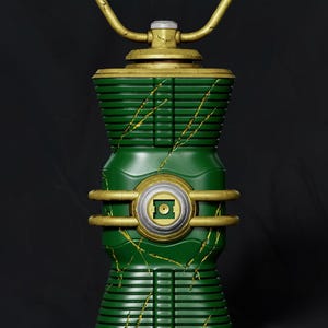 May include: A cylindrical green lantern with a gold handle and gold trim. The body features horizontal ridges, a central circular emblem with a square cutout, and gold-coloured cracks running vertically across the green surface.