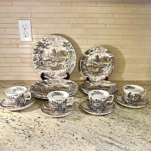 May include: A vintage tea set with plates, saucers, and teacups. The brown and white scenic landscape design decorates the plates, saucers, and teacups. The set includes large plates, smaller plates, and teacups with saucers.
