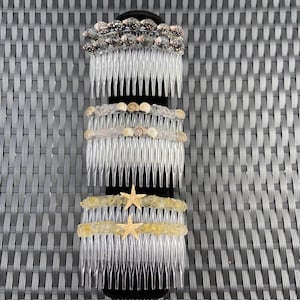Könnte beinhalten: Drei durchsichtige Plastikhaarkämme, die mit Muscheln verziert sind. Der obere Kamm hat schwarze und weiße Muscheln, der mittlere Kamm braune Muscheln und der untere Kamm goldene Seesterne.