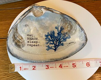 May include: A white seashell dish with a blue seaweed design and the text "eat. BEACH. sleep. repeat." printed on it. The dish is 4 inches wide.