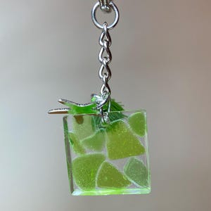 May include: A green resin keychain with a silver key ring. The resin is filled with small green pieces of glass.