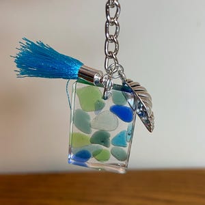 May include: A blue and green sea glass keychain with a silver charm and a blue tassel.