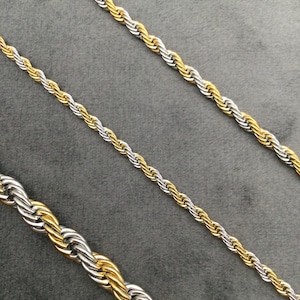 Puede incluir: Tres cadenas de cuerda doradas y plateadas de diferentes longitudes sobre un fondo gris.