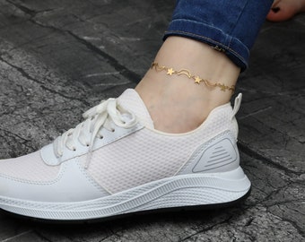 May include: A gold ankle bracelet with a crescent moon and star design. The bracelet is worn on a person's ankle with white sneakers and blue jeans.