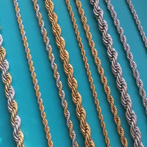 Op de afbeelding: Een verzameling touwkettingen die parallel zijn gerangschikt, met een mix van goudkleurige en zilverkleurige metalen afwerkingen. De kettingen variëren in dikte en vertonen een gedraaide, spiraalvormige textuur over de gehele lengte.
