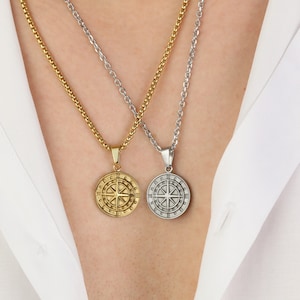 May include: Two necklaces with compass pendants. One necklace is gold with a gold compass pendant. The other necklace is silver with a silver compass pendant.