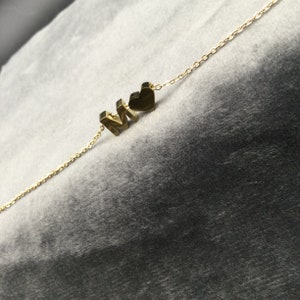 Peut inclure: Un collier en or avec un pendentif en forme de cœur et deux pendentifs en forme de lettre. Les lettres sont "M" et "M".