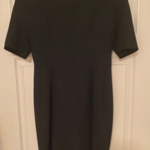 Könnte beinhalten: Ein schwarzes Kleid mit kurzen Ärmeln und quadratischem Ausschnitt. Das Kleid hat eine gerippte Textur und hängt an einem Holzbügel. Das Kleid ist einfarbig und scheint aus einem Strickstoff zu sein.