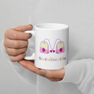 May include: White ceramic mug featuring a colourful graphic of two tea bags with raspberries and the text "Neurodiversitea".