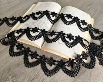 May include: Black lace trim with a scalloped edge and floral design. The trim is laying on a book with mathematical equations.