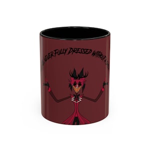 Puede incluir: Taza de cerámica granate con interior negro. La taza presenta un personaje de dibujos animados con un traje rojo con pajarita blanca y el texto "I'M NEVER FULLY DRESSED WITHOUT A SMILE" en letras negras. El personaje tiene una amplia sonrisa dentuda.