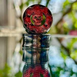 Puede incluir: Un par de dilatadores de oreja negros y rojos con un diseño de calavera y engranaje. El dilatador superior es rojo con un diseño de calavera y engranaje negro. El dilatador inferior es negro con un diseño de calavera y engranaje rojo.