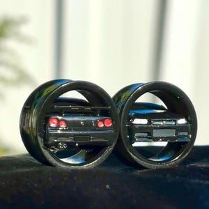 Peut inclure: Deux anneaux noirs avec un motif de voiture noire. L'anneau de gauche présente une vue arrière de la voiture avec des feux arrière rouges. L'anneau de droite présente une vue avant de la voiture avec des phares.