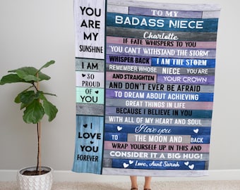 May include: A blue and pink blanket with a message for a niece. The text reads "To my badass niece Charlotte, if fate whispers to you... you can't withstand the storm. Whisper back, I am the storm. Remember whose niece you are and straighten your crown. And don't ever be afraid to dream about achieving great things in life because I believe in you with all of my heart and soul. I love you to the moon and back. Wrap yourself up in this and consider it a big hug! Love, Aunt Sarah"