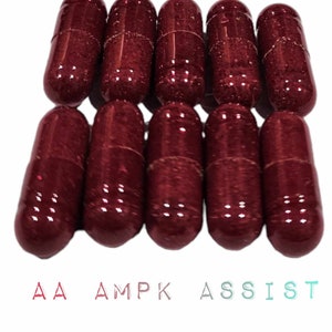 Puede incluir: Diez cápsulas de color granate dispuestas en dos filas. Las cápsulas son brillantes y tienen una superficie ligeramente texturizada. El texto "AA AMPK ASSIST" se muestra debajo de las cápsulas en un color degradado.