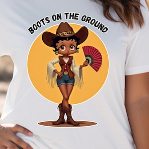 ウエスタンスタイルのブラックベティブーツオンザグラウンドユニセックスTシャツ、ラインダンスTシャツ、トレイルライドシャツ、カウボーイハットトップ、アフリカ系アメリカ人の服