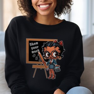 May include: Black sweatshirt with a cartoon image of a woman with glasses holding a pencil and a calculator. The woman is standing in front of a chalkboard with the words "Show your work" written on it.