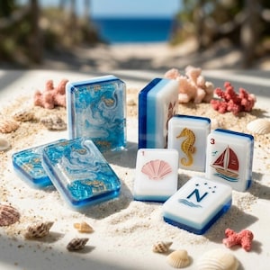 May include: A set of rectangular mahjong tiles featuring blue and white marbled resin designs with gold flakes, alongside white tiles decorated with a pink seashell, a yellow seahorse, a red sailboat, and the letter N with four stars.