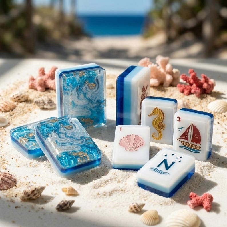 May include: A set of rectangular mahjong tiles featuring blue and white marbled resin designs with gold flakes, alongside white tiles decorated with a pink seashell, a yellow seahorse, a red sailboat, and the letter N with four stars.