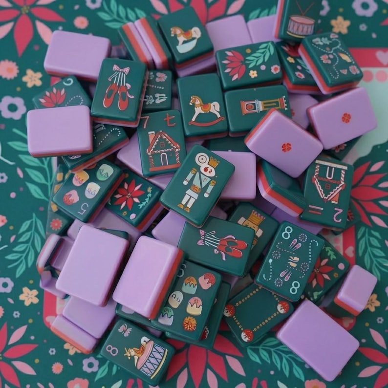 May include: A collection of rectangular mahjong tiles featuring a dark green base with festive illustrations including nutcrackers, ballet slippers, gingerbread houses, and rocking horses, interspersed with solid light purple tiles.