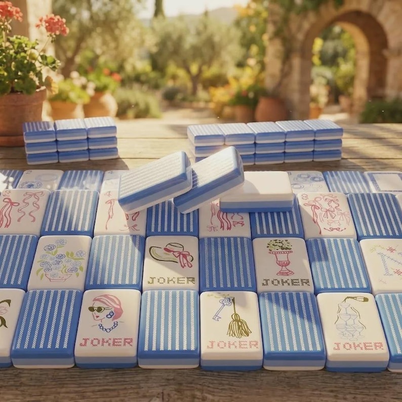 May include: A set of rectangular mahjong tiles featuring a blue and white striped pattern on the back. Some tiles display illustrations of flowers, hats, keys, and faces with the word JOKER printed below. Several tiles are stacked in rows.
