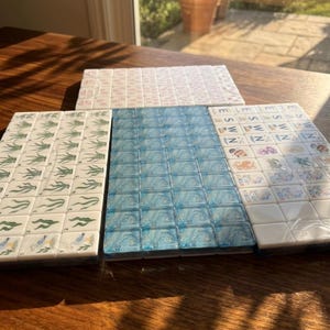 May include: A set of rectangular mahjong tiles arranged in three distinct groups. One group features green plant illustrations, another displays a blue swirled pattern, and the third shows various colorful icons and the letters E, S, W, and N.