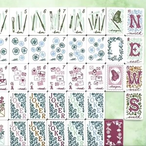 K&ouml;nnte beinhalten: Eine Sammlung von Mahjong-Steinen mit wei&szlig;en Vorderseiten und verschiedenen Illustrationen, darunter Kunstbedarf, Blumen, Umschl&auml;ge, Schmetterlinge und Richtungsbuchstaben. Die Steine zeigen Zahlen, chinesische Schriftzeichen und das Wort Joker in Blumenmustern.