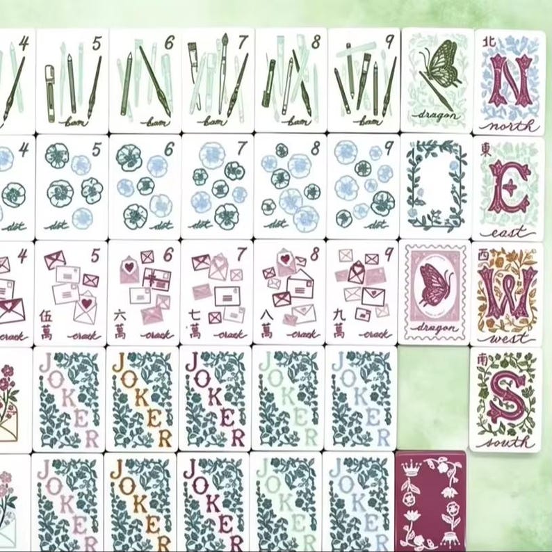 K&ouml;nnte beinhalten: Eine Sammlung von Mahjong-Steinen mit wei&szlig;en Vorderseiten und verschiedenen Illustrationen, darunter Kunstbedarf, Blumen, Umschl&auml;ge, Schmetterlinge und Richtungsbuchstaben. Die Steine zeigen Zahlen, chinesische Schriftzeichen und das Wort Joker in Blumenmustern.