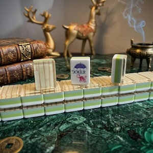 May include: A set of rectangular mahjong tiles arranged in rows, featuring a layered design with a white top, a light green middle, and a translucent base. One tile displays a purple umbrella graphic above the red text JOKER and a red monkey.