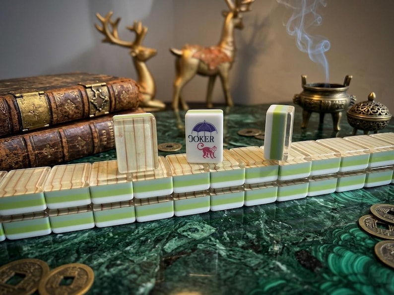 May include: A set of rectangular mahjong tiles arranged in rows, featuring a layered design with a white top, a light green middle, and a translucent base. One tile displays a purple umbrella graphic above the red text JOKER and a red monkey.