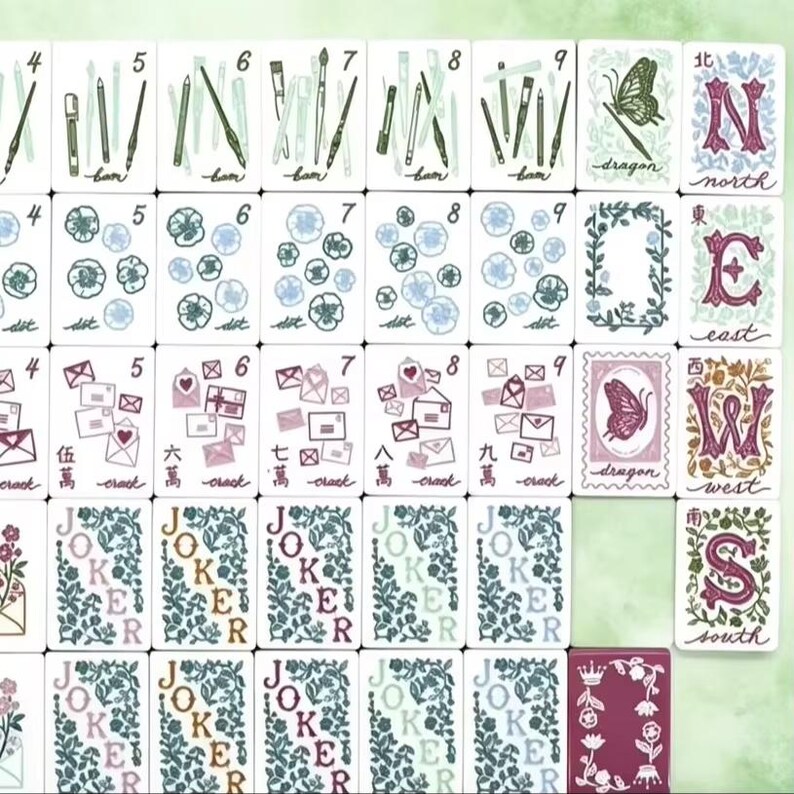 May include: A collection of mahjong tiles featuring white faces with various illustrations including art supplies, flowers, envelopes, butterflies, and directional letters. The tiles display numbers, Chinese characters, and the word Joker in floral patterns.