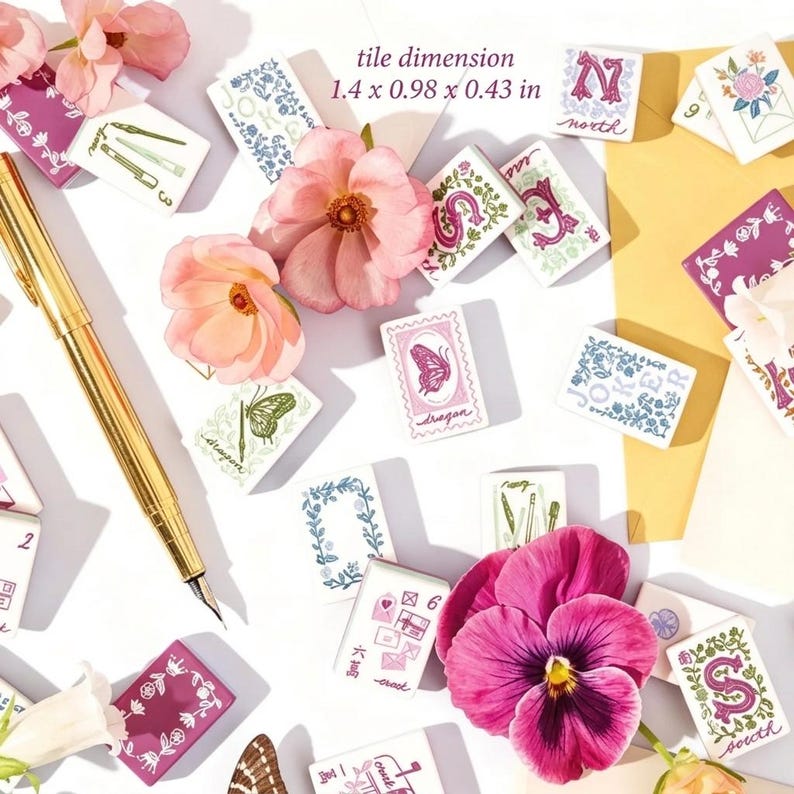 K&ouml;nnte beinhalten: Eine Sammlung rechteckiger Kacheln mit verschiedenen Blumen-, Buchstaben- und Schmetterlingsillustrationen, begleitet von einem goldenen F&uuml;llfederhalter und rosa Bl&uuml;ten. Die Kacheln messen 3,56 x 2,49 x 1,09 cm, wie im Text angegeben.